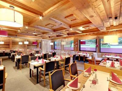 Moderner, gemütlicher Gastraum mit Holzwänden, vielen Holztischen, schwarzen Stühlen und großen Fenstern.