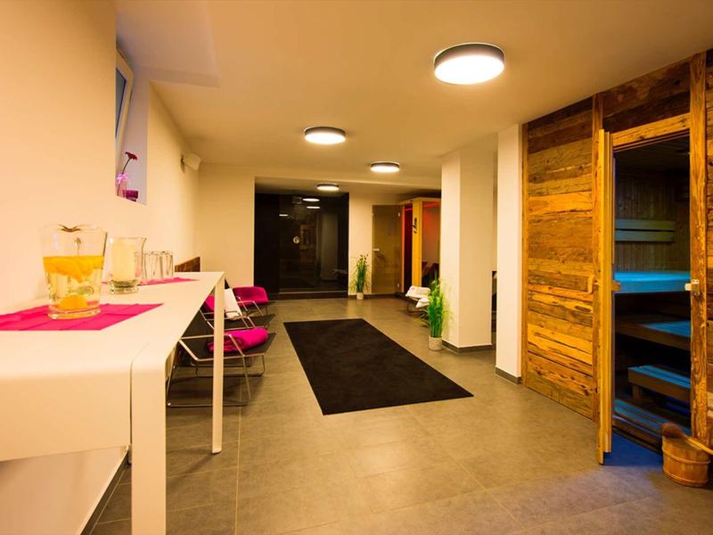 Heller Flur mit Holzsauna, weißen Wänden, grauem Boden und mehreren Deckenlampen.