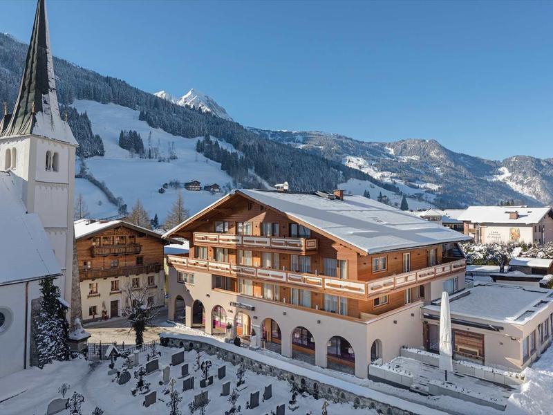 Winterliche Berglandschaft mit verschneiten Holzhäusern und Kirche unter klarem Himmel.
