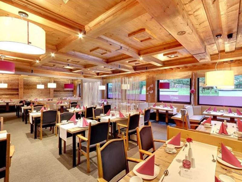 Moderner, gemütlicher Gastraum mit Holzwänden, vielen Holztischen, schwarzen Stühlen und großen Fenstern.