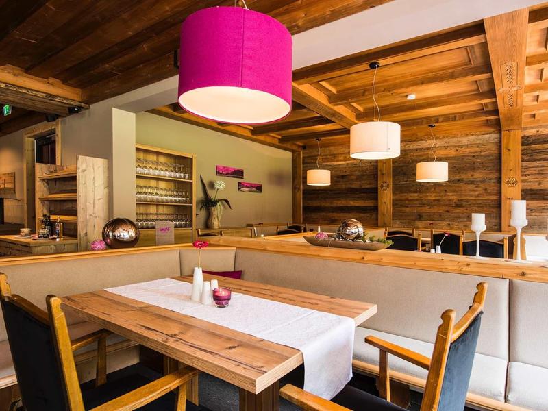 Gemütliches Restaurant mit Holztischen, Stühlen und warmem Holzdekor, beleuchtet von bunten Lampen.