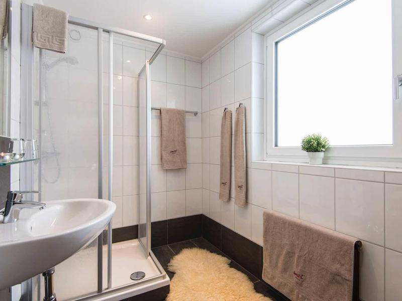 Kleines weiß gekacheltes Badezimmer mit Dusche, Waschbecken, Fenster und beigen Handtüchern.