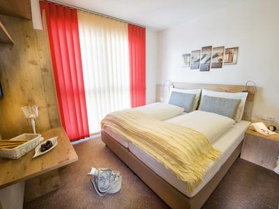 Lichte hotelkamer met tweepersoonsbed, rode gordijnen en modern houten meubilair.