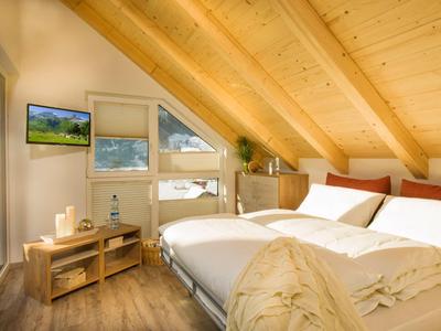 Gezellige slaapkamer met houten balkenplafond, tweepersoonsbed en tv onder schuine dak.