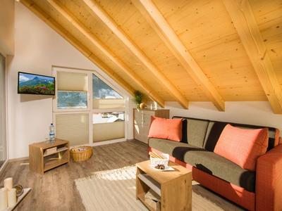 Gezellige woonkamer met schuine houten plafond, bank en groot raam met uitzicht op de bergen.