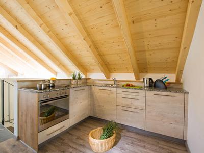 Moderne keuken onder een schuine houten plafond met lichte kasten en houten vloer.