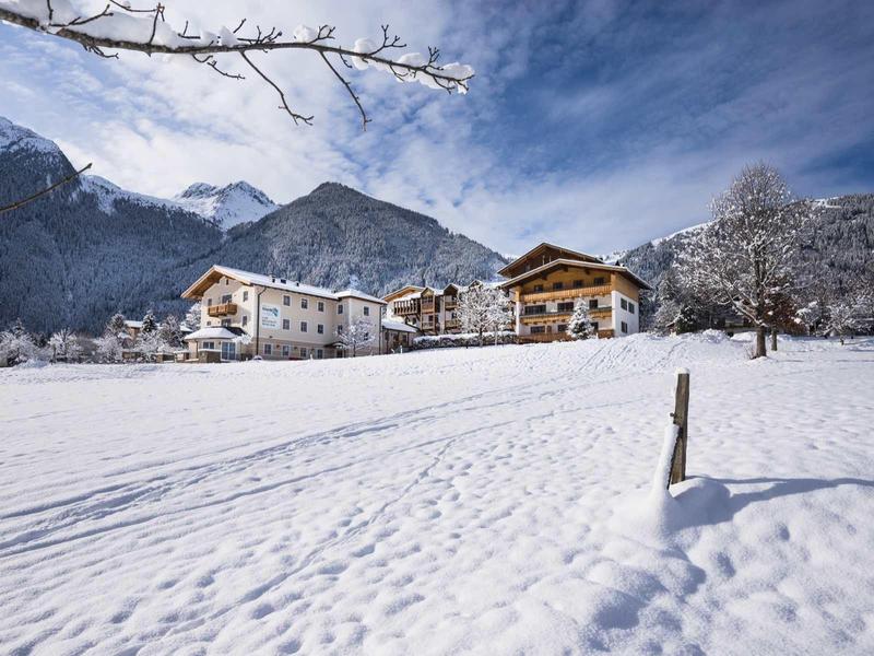 Paysage enneigé avec des hôtels devant des montagnes nuageuses et un ciel bleu.