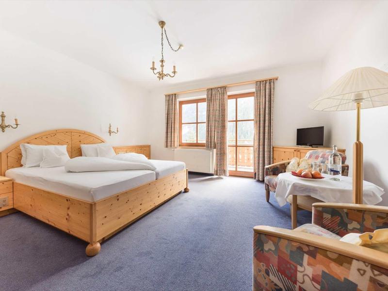 Chambre d'hôtel lumineuse avec mobilier en bois, lit double, coin salon et balcon avec vue extérieure.