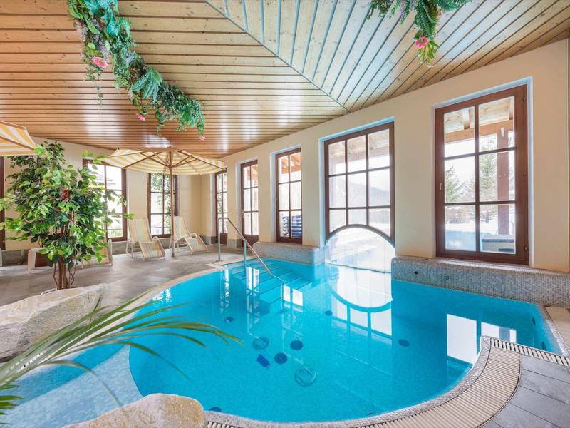 Piscine intérieure avec plafond en bois, grandes fenêtres et plantes dans l'espace bien-être.