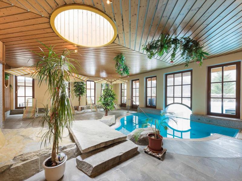 Espace piscine intérieure avec plafond en bois, plantes et sièges relaxants dans un hôtel.