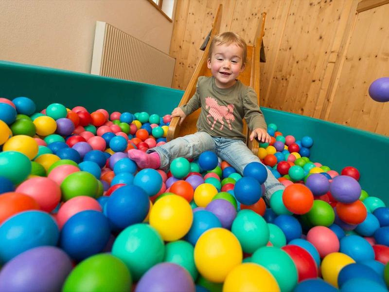 Enfant jouant gaiement dans une piscine à balles colorée dans un intérieur en bois.
