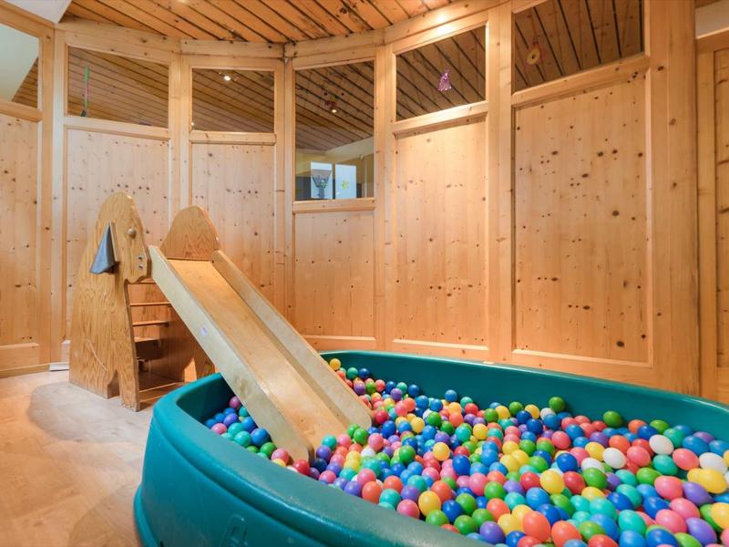 Espace intérieur avec toboggan en bois et piscine à balles colorée dans une pièce conviviale.