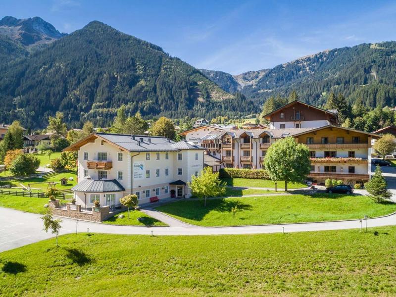 Complexe hôtelier avec bâtiments de style chalet dans un paysage montagneux vert sous un ciel bleu.