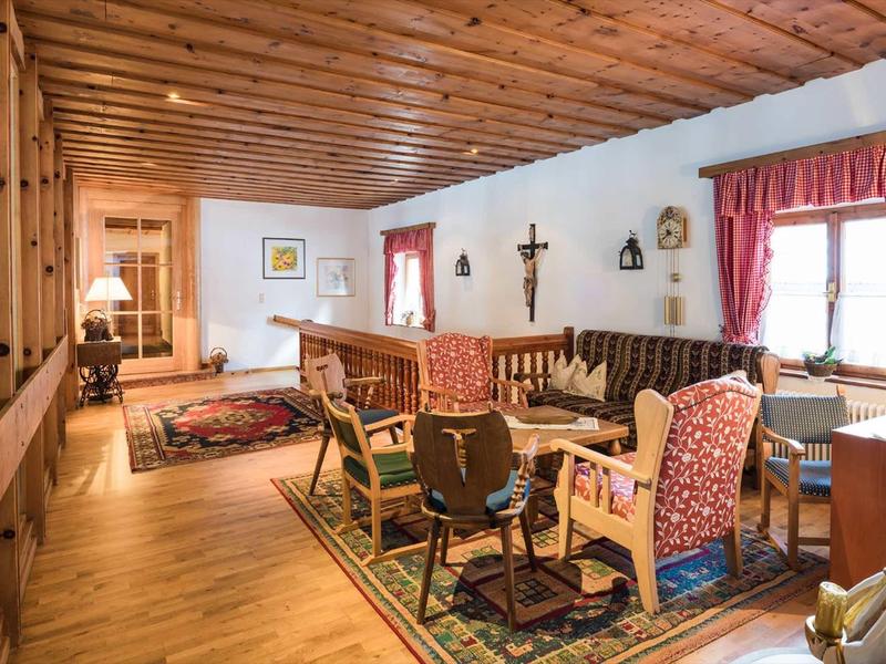 Salon avec plafond en bois rustique, coin salon, tapis et grandes fenêtres avec rideaux rouges.