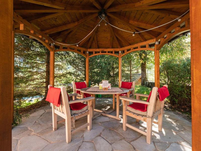Kiosque en bois avec table ronde et chaises, entouré de nature verte en plein air.