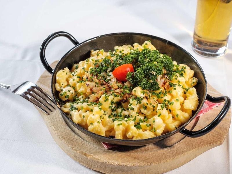 Bol de spaetzle au bacon, garni d'herbes, à côté d'un verre de bière.