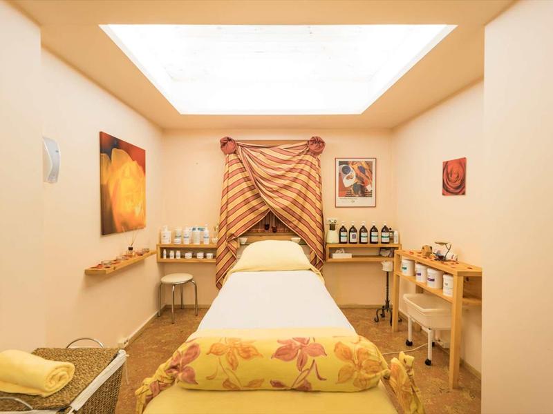 Salle de bien-être lumineuse avec table de massage, rideau décoratif et tons chauds.