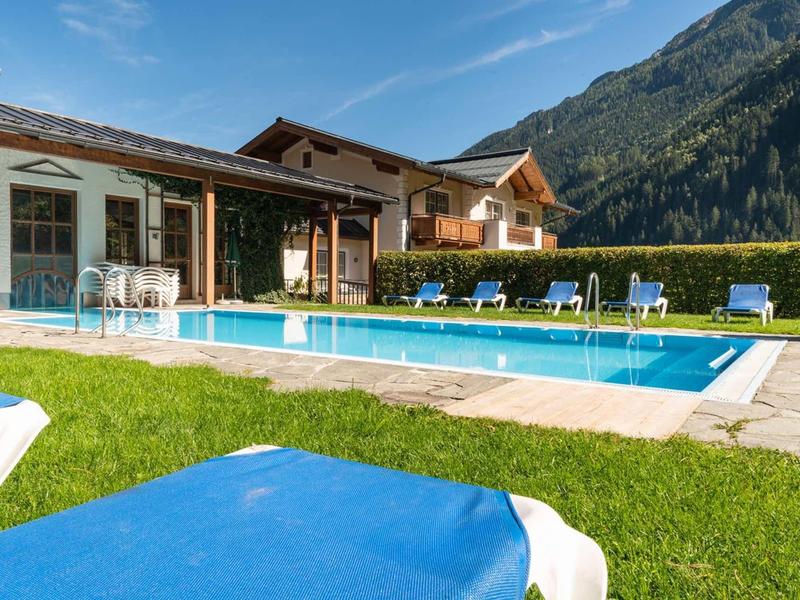 Hôtel avec piscine extérieure, chaises longues et paysage montagneux sous un ciel clair.