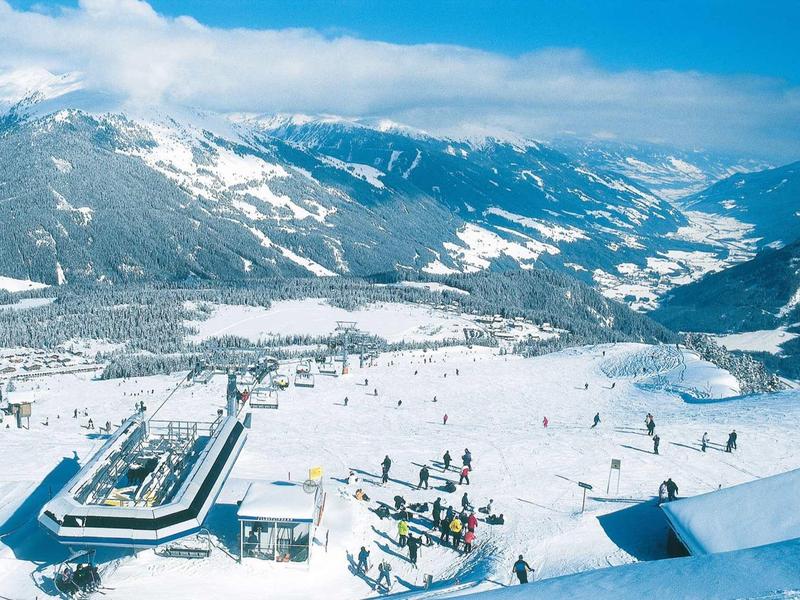 Vue sur des montagnes enneigées et un hôtel avec des skieurs dans la vallée sous un ciel clair.