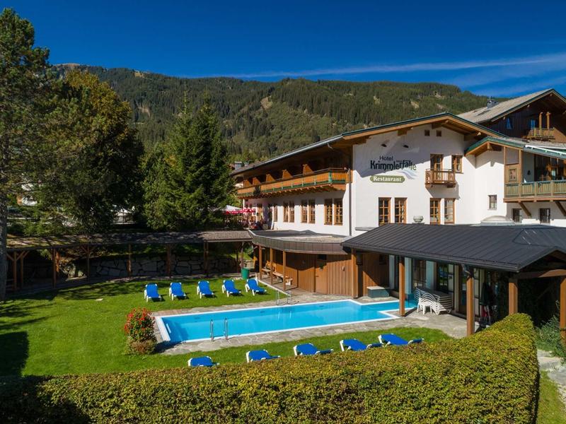 Hôtel avec piscine extérieure, chaises longues et montagnes en arrière-plan par jour ensoleillé.