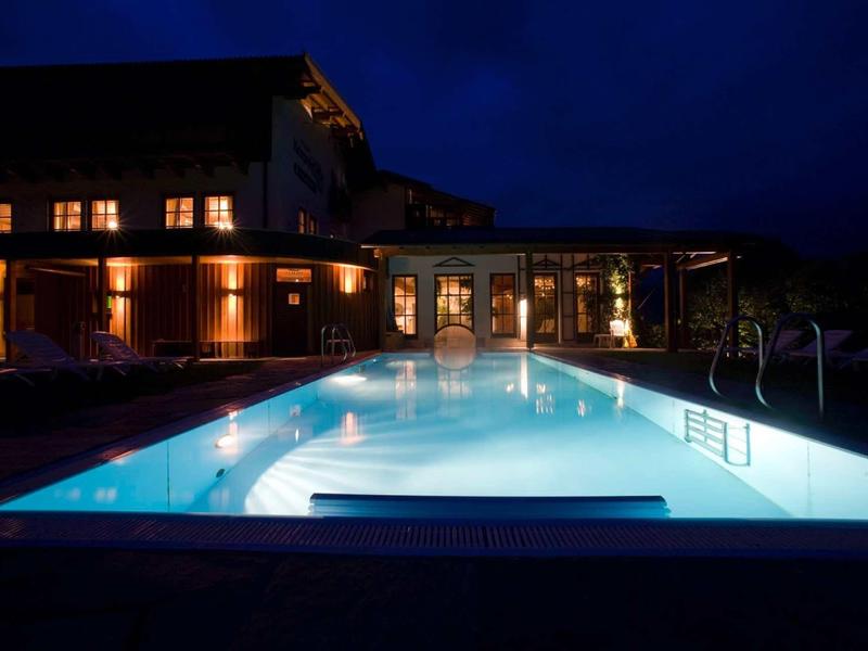Piscine extérieure illuminée à côté de l'hôtel dans un cadre nocturne calme.