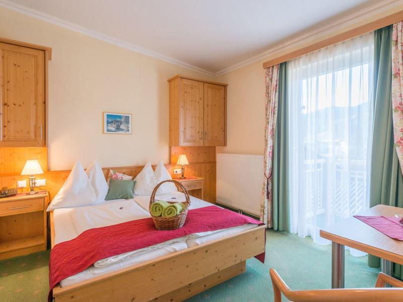 Przytulny pokój hotelowy z podwójnym łóżkiem, drewnianymi meblami i balkonem z zasłonami.