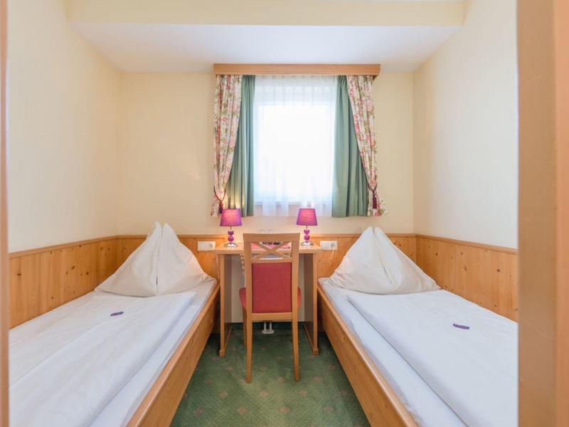 Mały pokój hotelowy z dwoma pojedynczymi łóżkami, biurkiem i oknem z zasłonami.