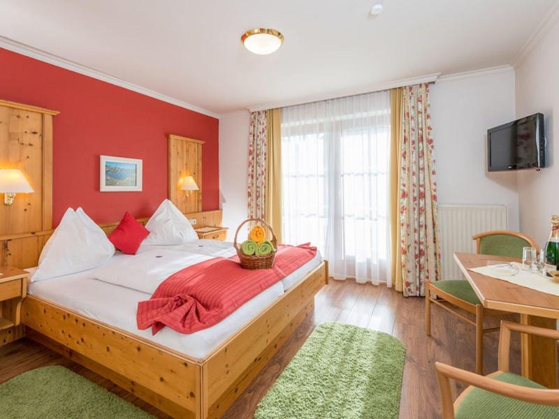 Przytulny pokój hotelowy z podwójnym łóżkiem, drewnianymi meblami i balkonowym oknem z zasłonami.