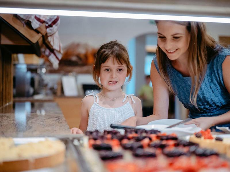 Mała dziewczynka i kobieta patrzą na różne ciasta w cukierni.