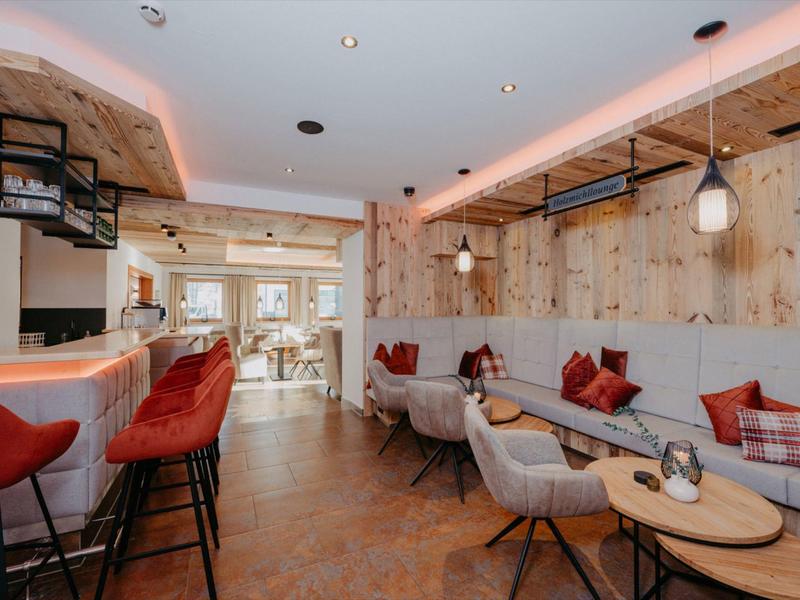 Przytulny bar hotelowy z czerwonymi hokerami, drewnianymi ścianami, nowoczesnym oświetleniem i miejscami do siedzenia.