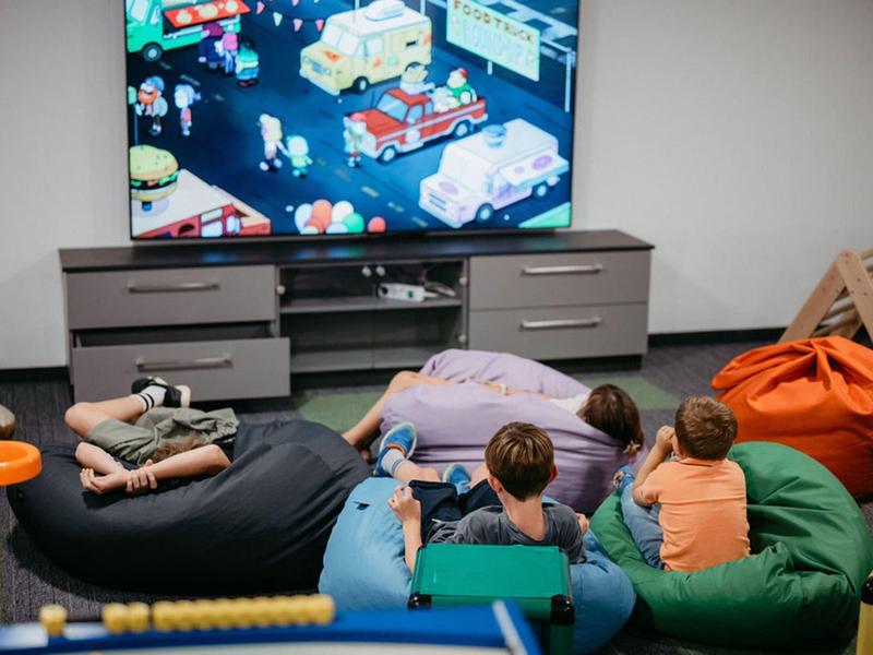 Kilka osób relaksuje się na dużych pufach przed telewizorem w salonie.