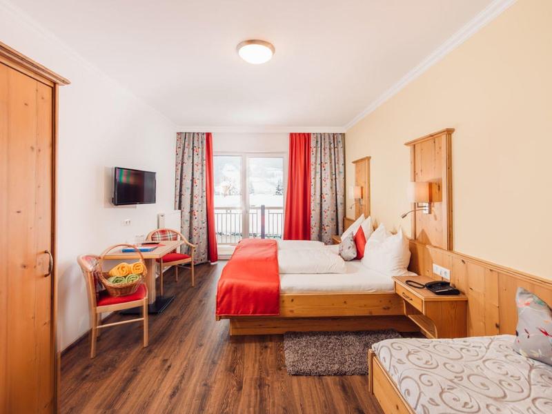 Przytulny pokój hotelowy z łóżkiem podwójnym, szafą, telewizorem i balkonem z zasłonami.