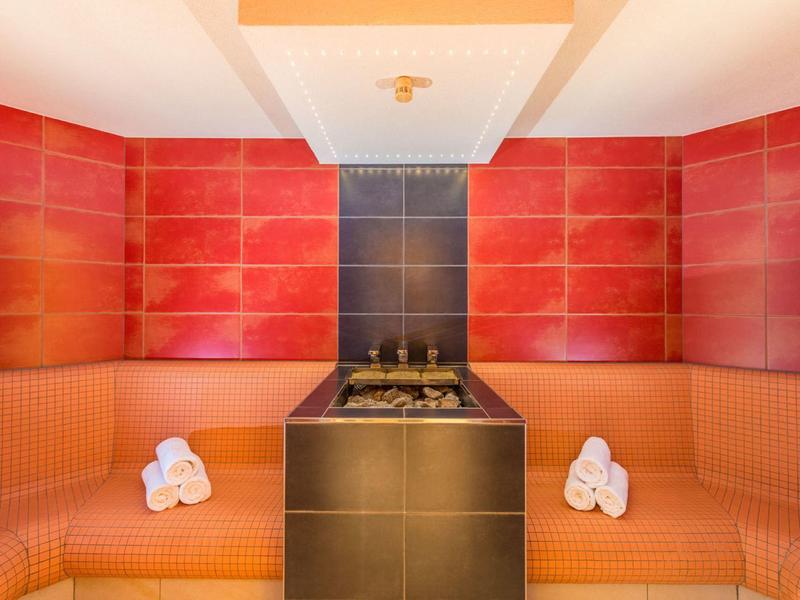 Nowoczesny pokój wellness z czerwonym wzorem na ścianie, brązowymi ławkami i średniej wielkości czarnym stołem.