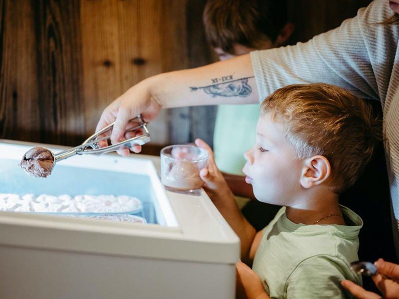 Dziecko nabiera lody z zamrażarki podczas wakacji z pomocą dorosłego.