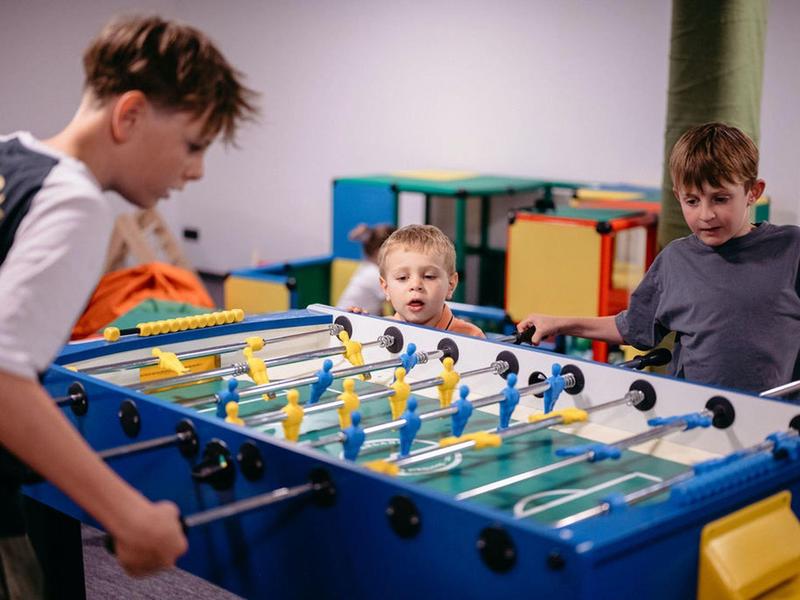 Trzech chłopców gra razem przy niebieskim stole do piłkarzyków w kolorowym pokoju.