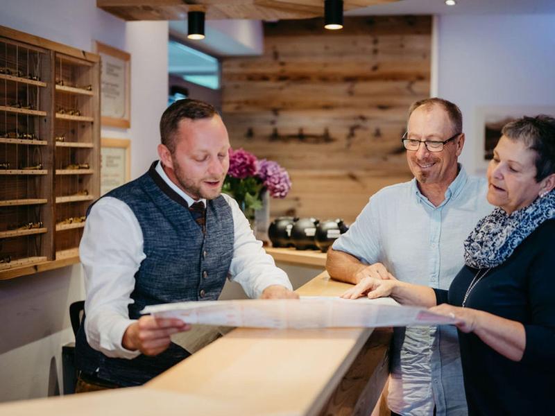 Trzy osoby rozmawiające przy recepcji, mężczyzna pokazuje dokument.