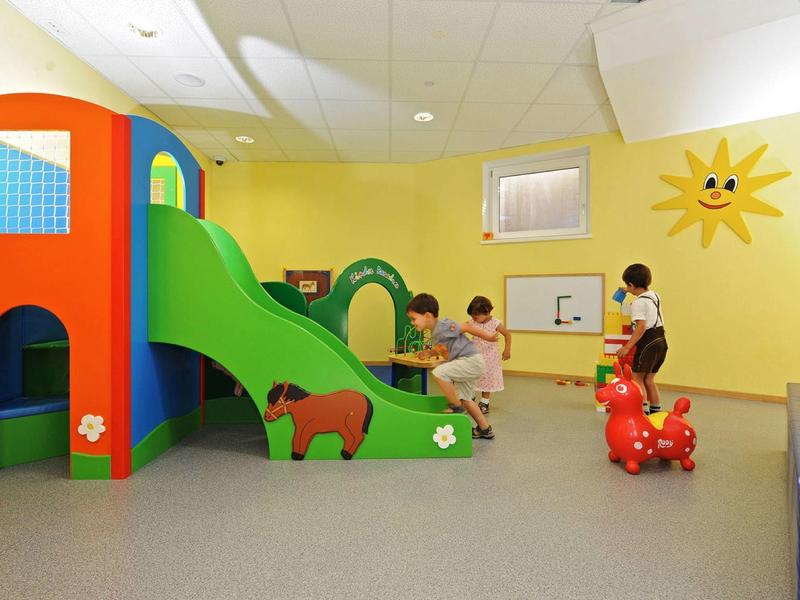 Děti si hrají v barevné vnitřní herně se skluzavkou a hračkami.