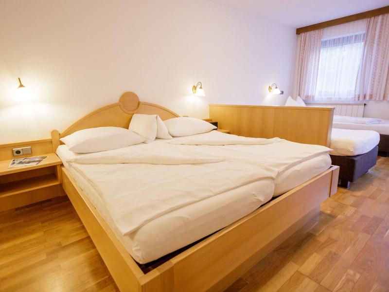 Světly hotelový pokoj se dvěma manželskými postelemi, dřevěnou podlahou a moderním osvětlením.