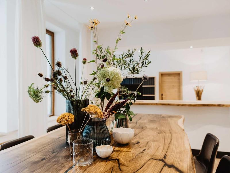 Rustykalny drewniany stół z różnymi kwiatowymi aranżacjami w jasnym pomieszczeniu.