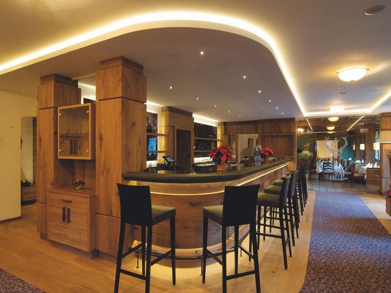 Strefa baru w hotelu z drewnianym kontuarem i czarnymi stołkami barowymi, ciepłe oświetlenie.