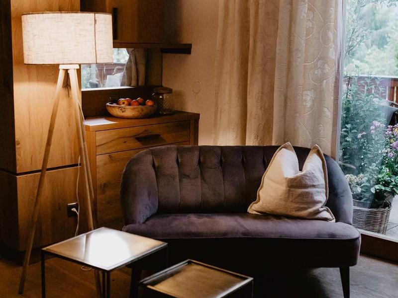 Przytulny kącik wypoczynkowy z ciemną sofą, poduszkami, dwoma stolikami bocznymi i lampą stojącą o ciepłym świetle.