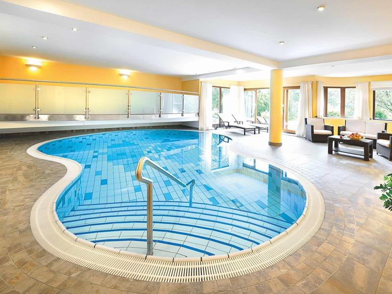 Basen kryty o zaokrąglonym kształcie, niebieskie płytki i miejsce do siedzenia przy oknie.