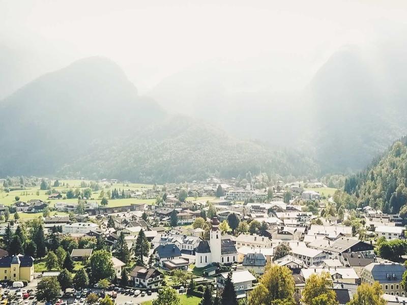 Panorama małej górskiej wioski w dolinie z otaczającymi zalesionymi górami i mglistym niebem.