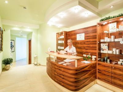 Réception dans un hôtel lumineux avec comptoir en bois et employée accueillante.