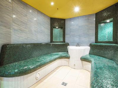 Salle de détente confortable avec bancs incurvés en mosaïque verte et plafond jaune dans un spa.