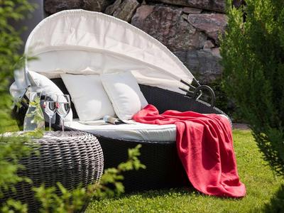 Coin lounge confortable avec coussins et couverture rouge dans le jardin à côté des rochers.