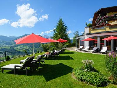 Chaises longues avec parasols rouges sur pelouse verte devant un hôtel avec vue sur la montagne.