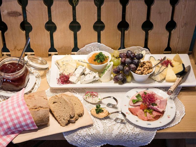 Plateau de petit déjeuner avec pain, charcuterie, fromage, fruits et confiture sur une table.