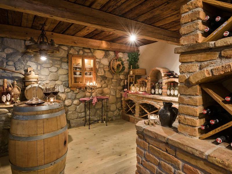 Cave à vin rustique avec poutres en bois, murs en pierre, étagères et baril à vin.