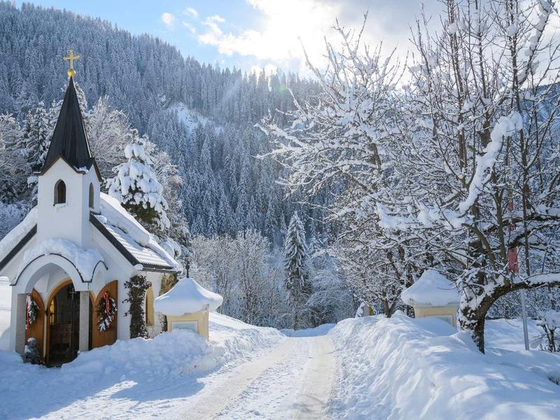 Chapelle enneigée et chemin enneigé dans un paysage montagneux hivernal.